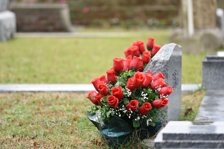 A bouquet of fresh red roses interspersed with small white filler flowers and green foliage, arranged in a rounded floral display. The bouquet is wrapped in dark green and transparent plastic, resting